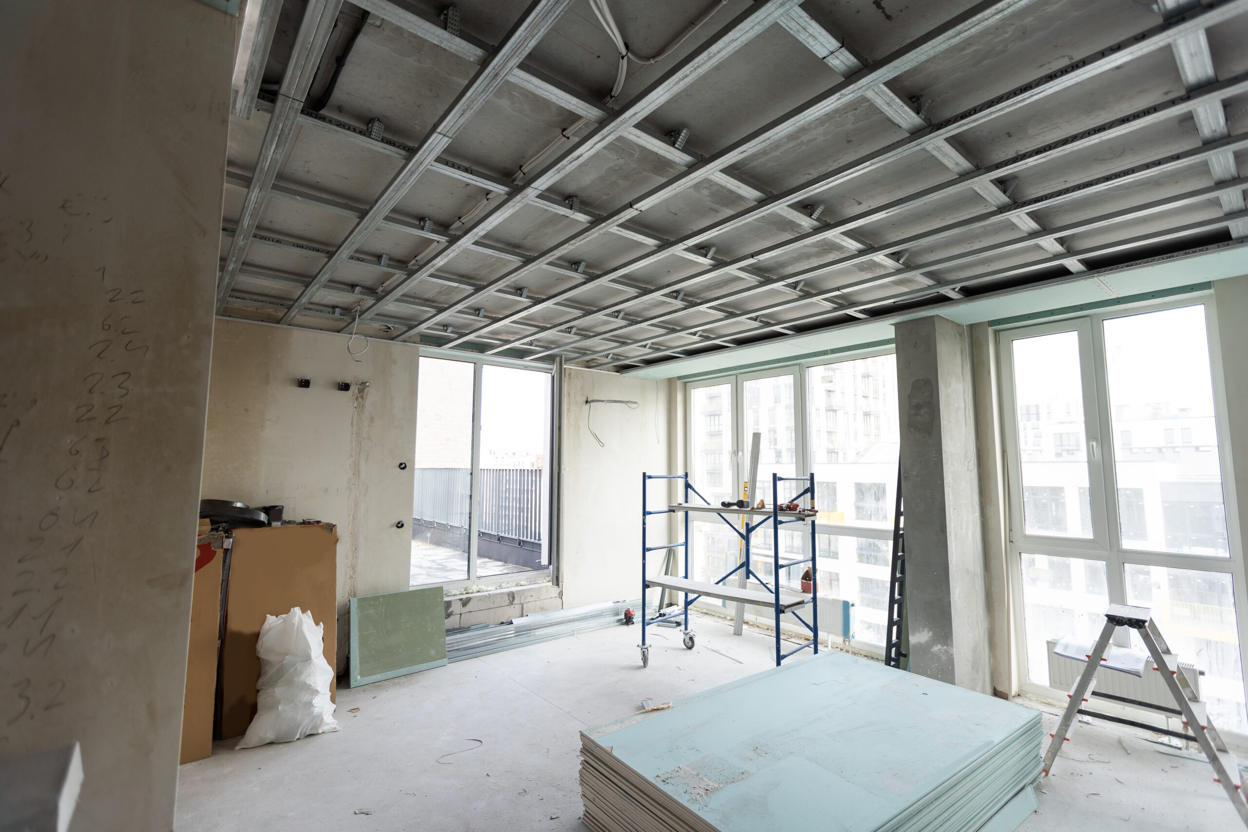 Interior de uma construção em andamento. Com grandes janelas de vidro, andaimes, escadas.