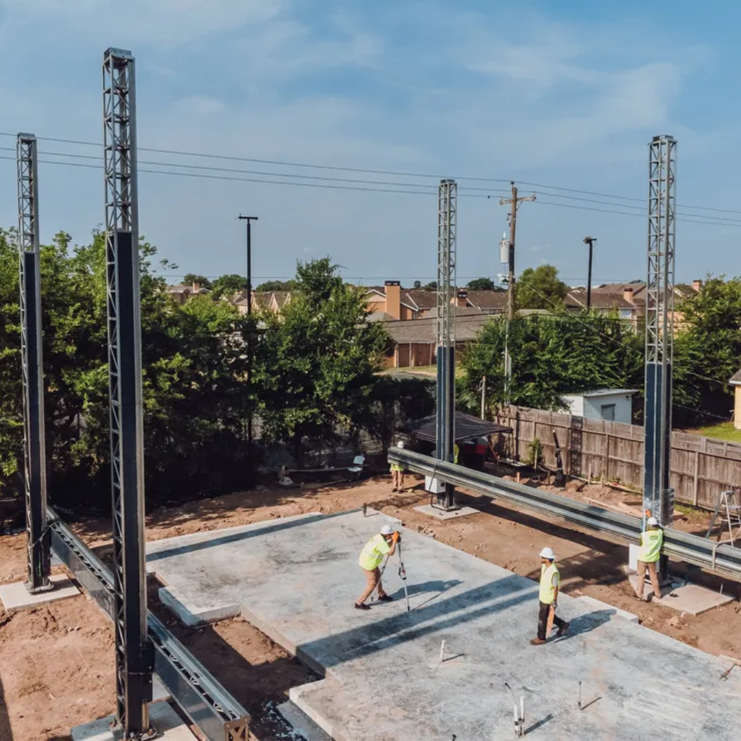 Construção de uma casa utilizando tecnologia de impressão 3D, com trabalhadores ajustando a base de concreto e estrutura metálica ao redor da área da obra